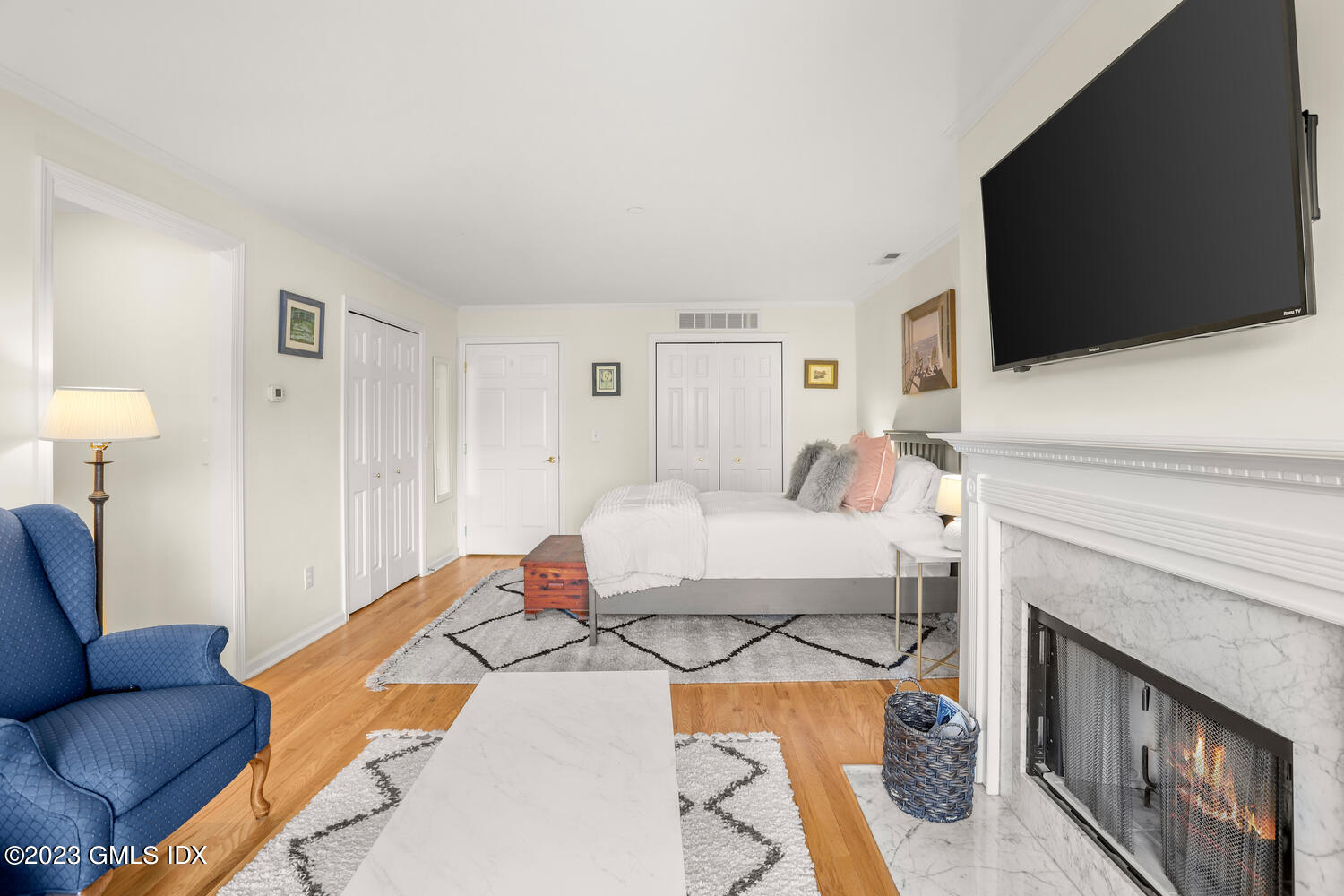 Furnished bedroom with a marble fireplace, wall-mounted television, white bed, and blue armchair.