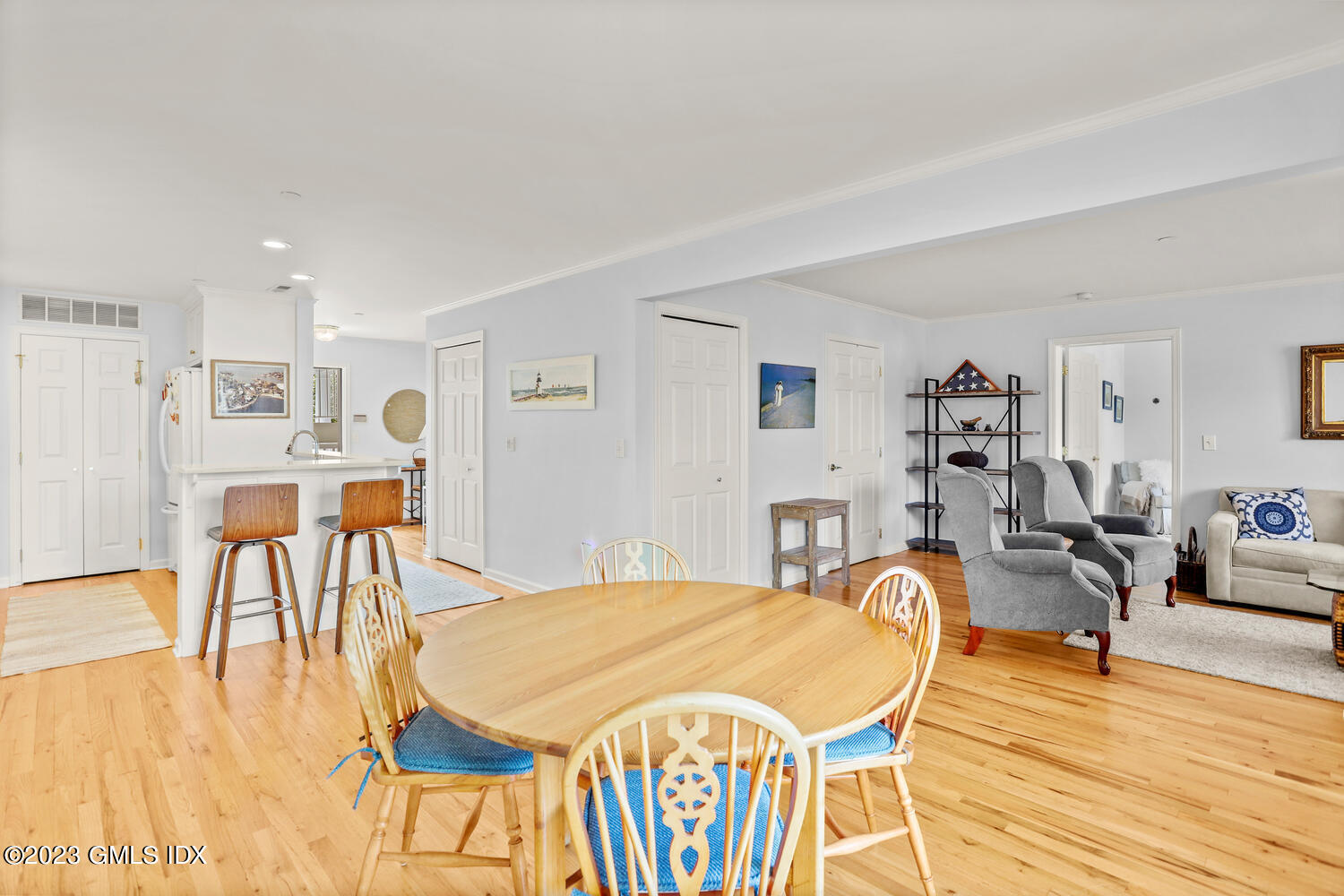 Open-plan dining and living area with hardwood floors, a wood dining table, kitchen breakfast bar, and gray armchairs.