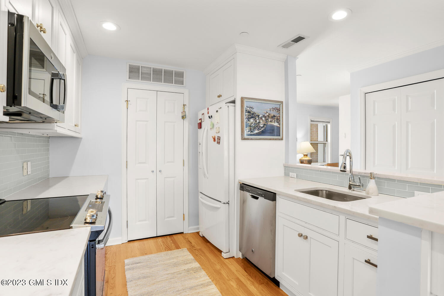 Bright kitchen with white cabinets, stainless steel appliances, pale countertops, and hardwood floors.