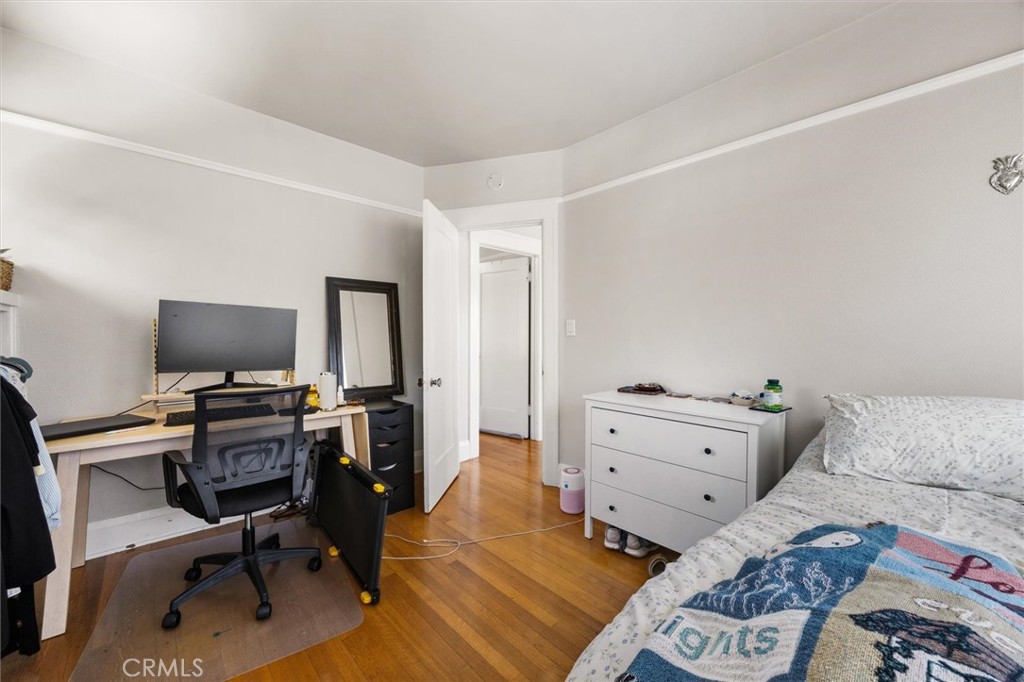 Bedroom with a bed, white dresser, and desk and office chair on wood flooring.