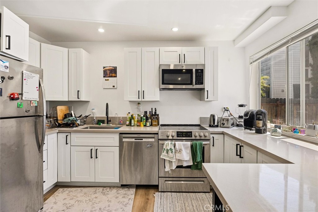 Kitchen with white cabinets, stainless steel appliances, and a large peninsula beside wide windows.