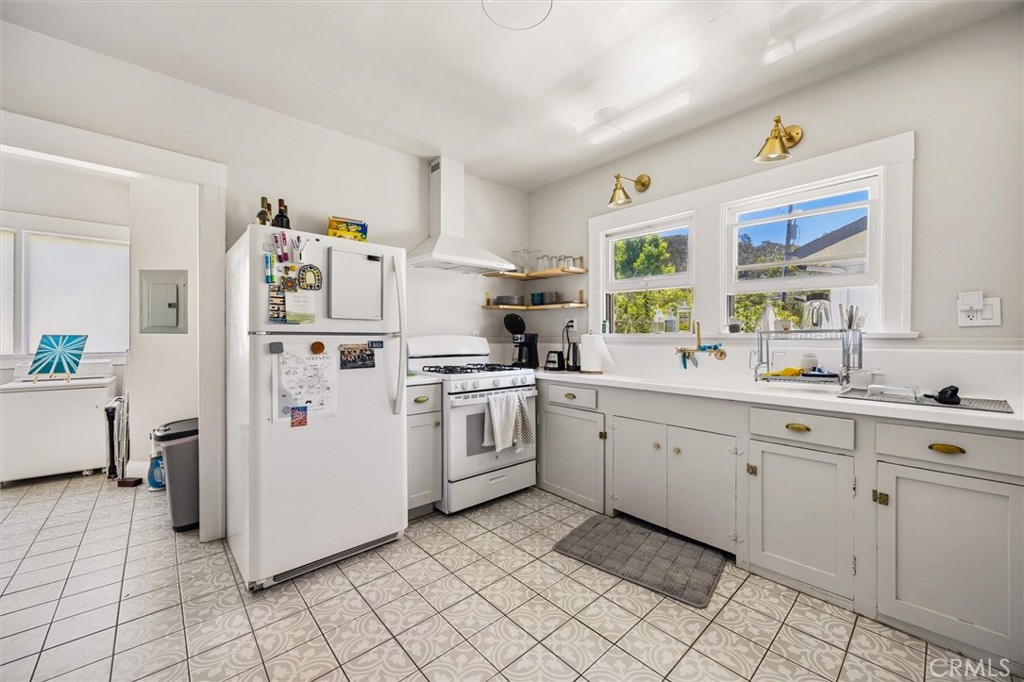 Bright kitchen with white cabinets, gas range, large windows, and patterned tile flooring.