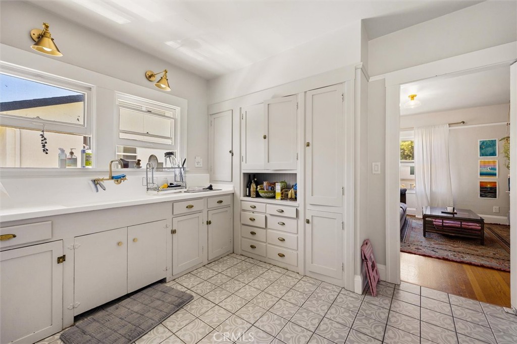 White kitchen with paneled cabinets, patterned tile floor, and an open doorway to the living room.
