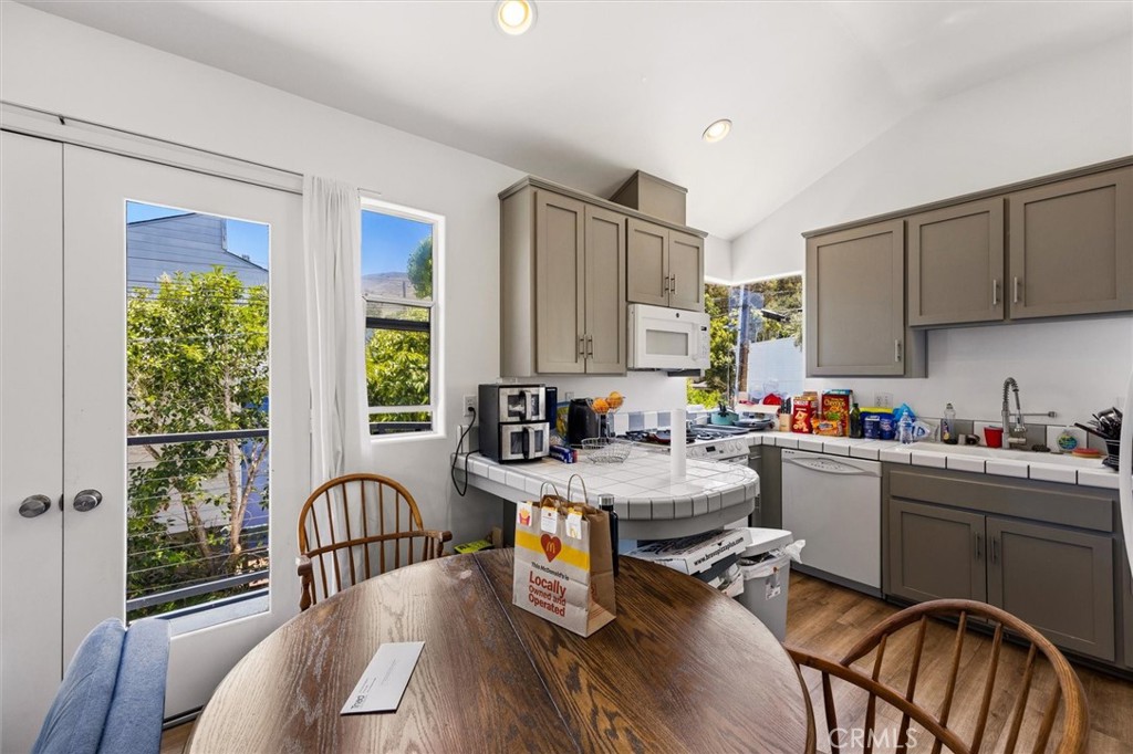 Kitchen with taupe cabinets, a rounded tile peninsula, and a wooden dining table by tall windows.