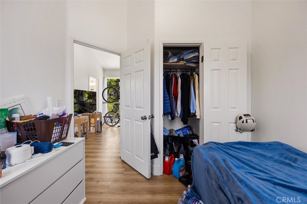 Bedroom with a blue-covered bed, open clothes closet, and a crowded white dresser.