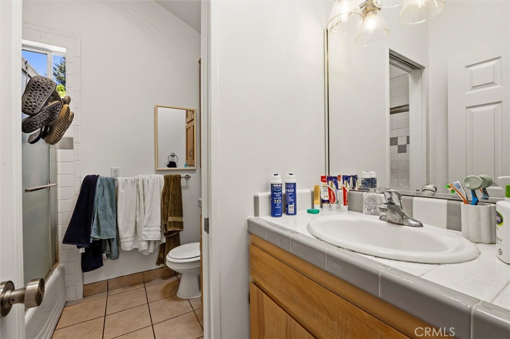 Bathroom with a white tiled sink counter, wood vanity, and shower-tub enclosure.