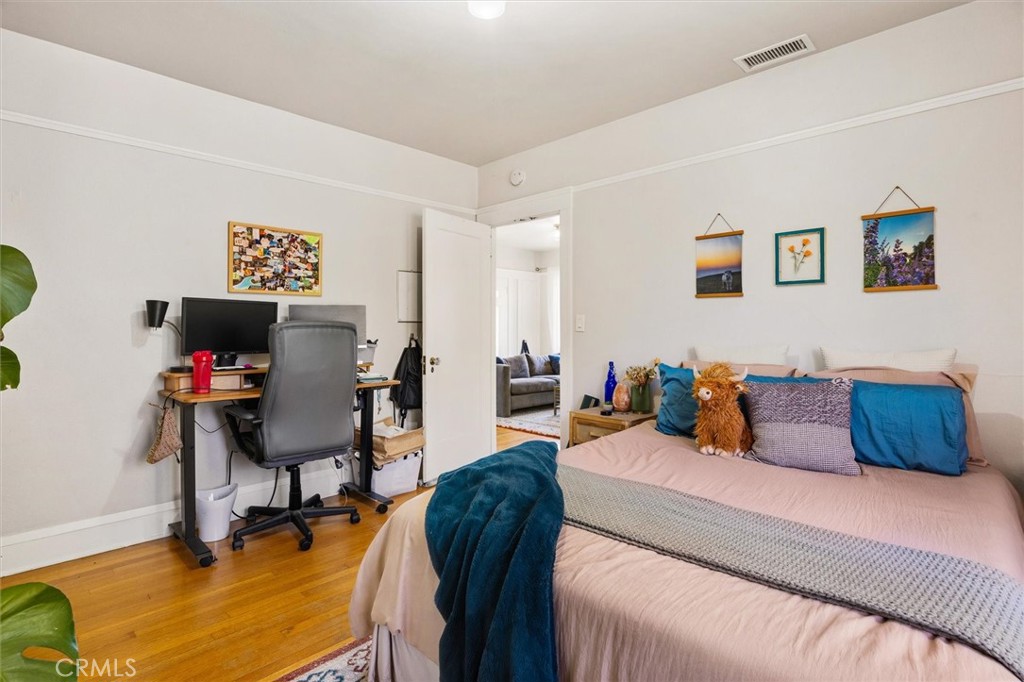 Furnished bedroom with blush-pink bedding, teal accents, a desk, and hardwood floors.