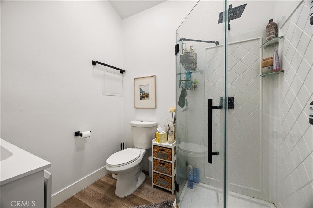 Bathroom with a glass shower, white diamond-pattern tile, toilet, and wood-look flooring.