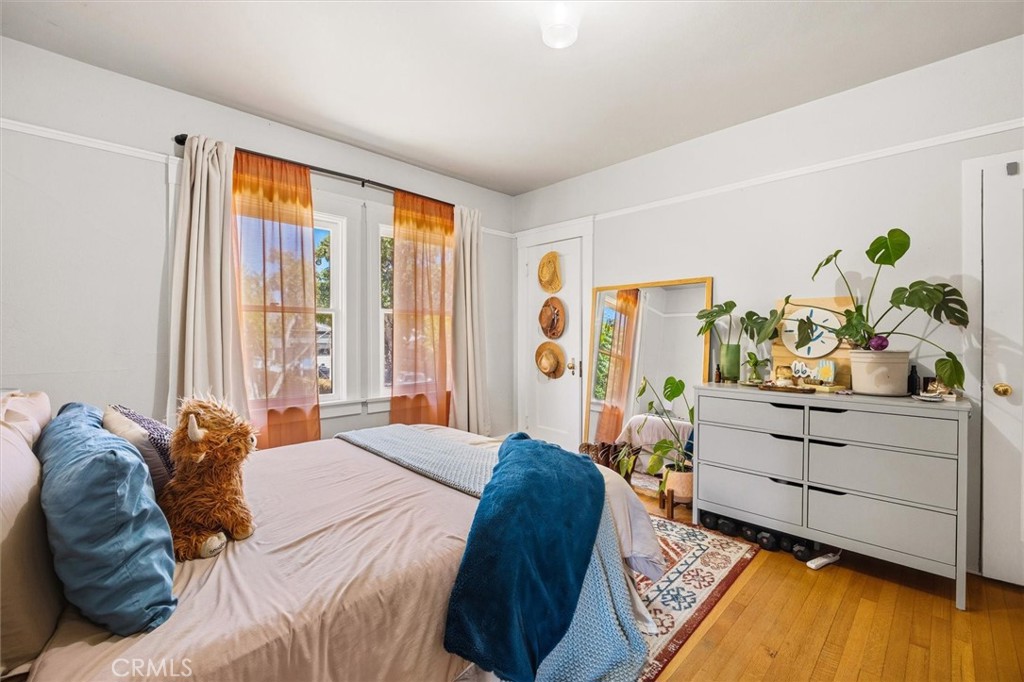 Furnished bedroom with orange-curtained windows, a white dresser, plants, and hardwood floors.