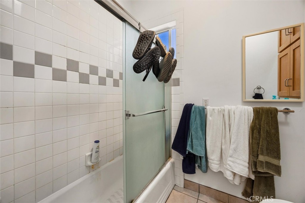 Bathroom with a tiled tub and shower, frosted glass door, gray accent tiles, hanging towels, and mirror.