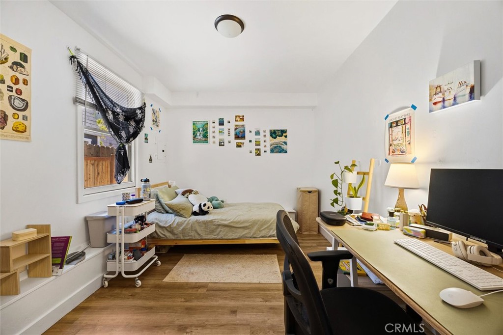 Bedroom with a bed, desk and computer, wall art, and wood flooring.