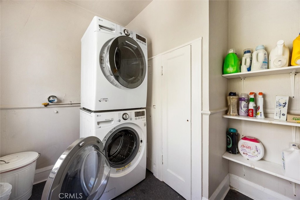Laundry room with stacked front-loading washer and dryer and shelves of cleaning supplies.