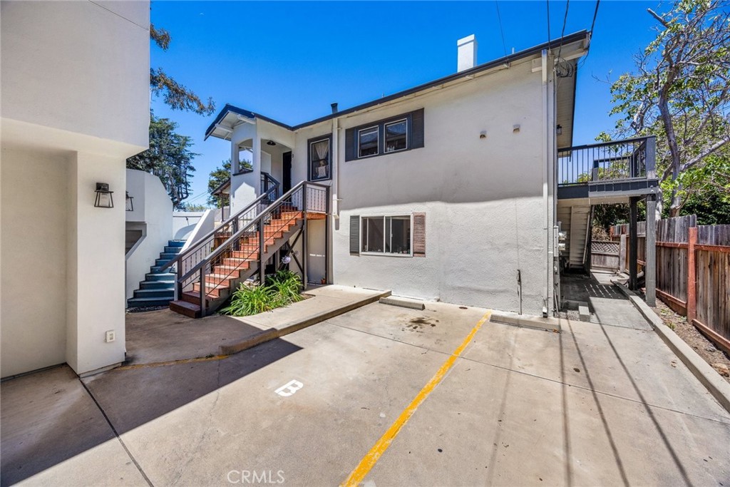 White multi-unit building with exterior staircases, an upper balcony, and parking spaces.