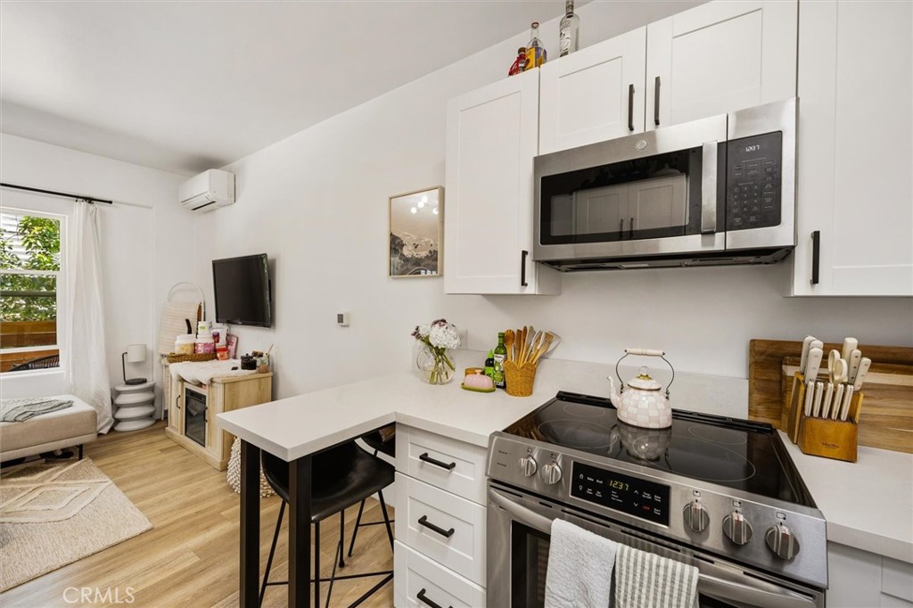 Furnished kitchen with white cabinets, stainless steel appliances, and a peninsula with bar seating.