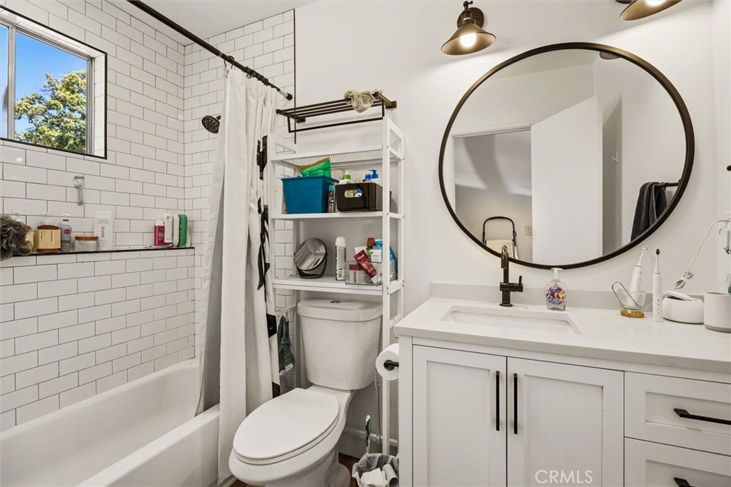 Bathroom with white subway tile around the tub and a white vanity beneath a large round mirror.
