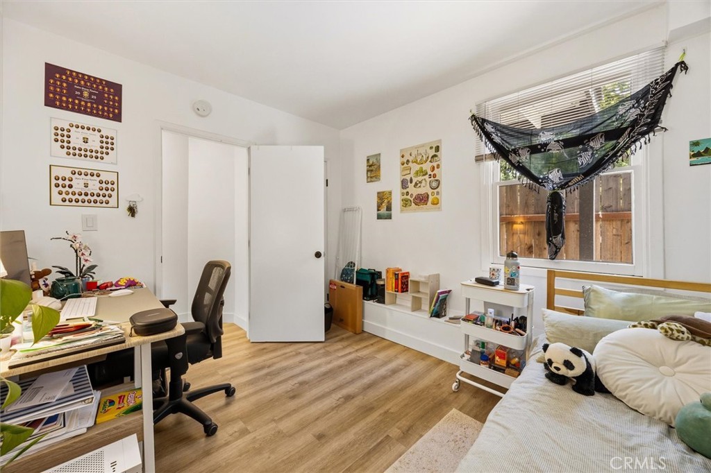 Bedroom with a desk, wood-look flooring, and a black hammock hanging by the window.