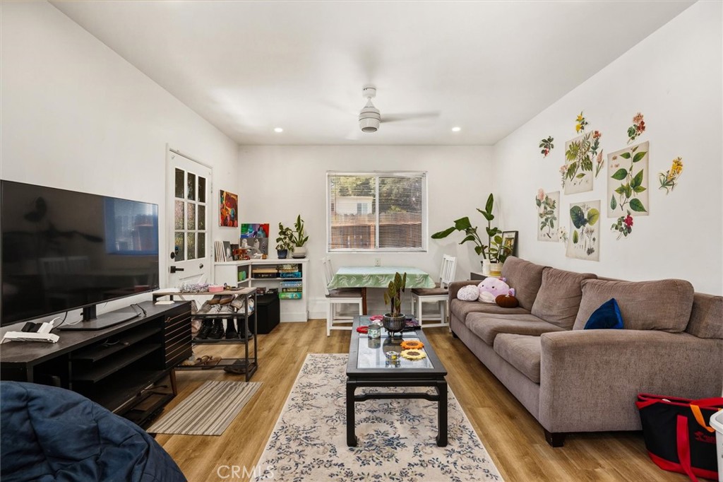 Furnished living room with a beige sectional, botanical wall art, and a small dining table by the window.