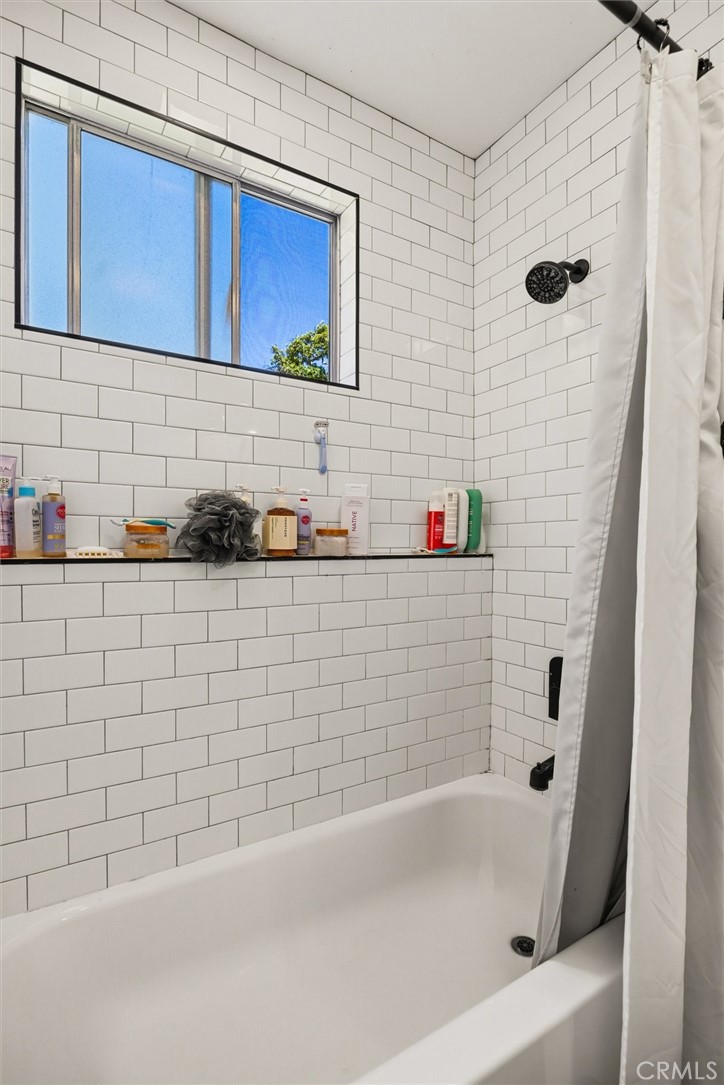 Bathroom with a white bathtub, subway tile walls, and a high window above the shower.