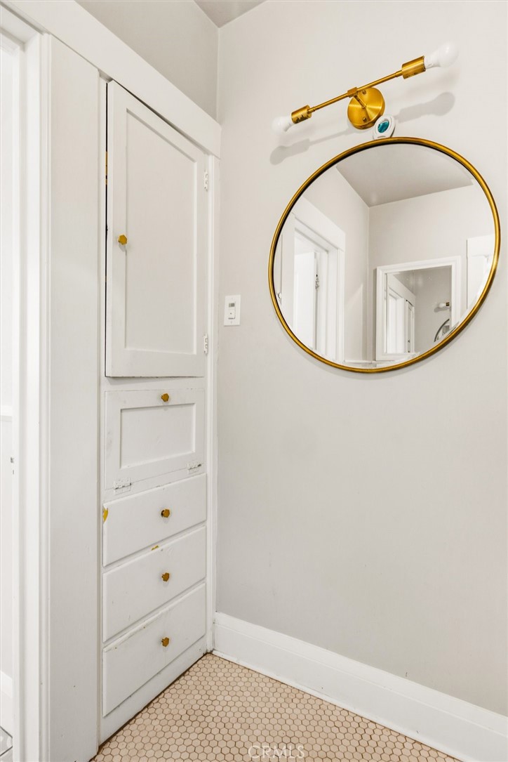 Bathroom with built-in white cabinetry, a round gold-framed mirror, and hexagonal tile flooring.