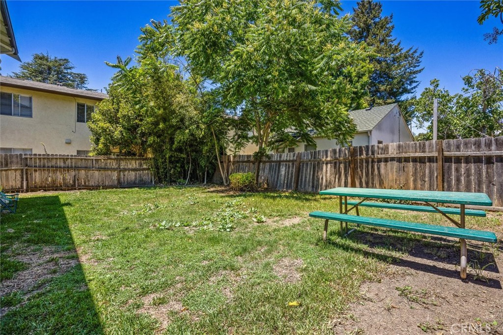 Fenced backyard with mature trees, lawn, and a green picnic table.