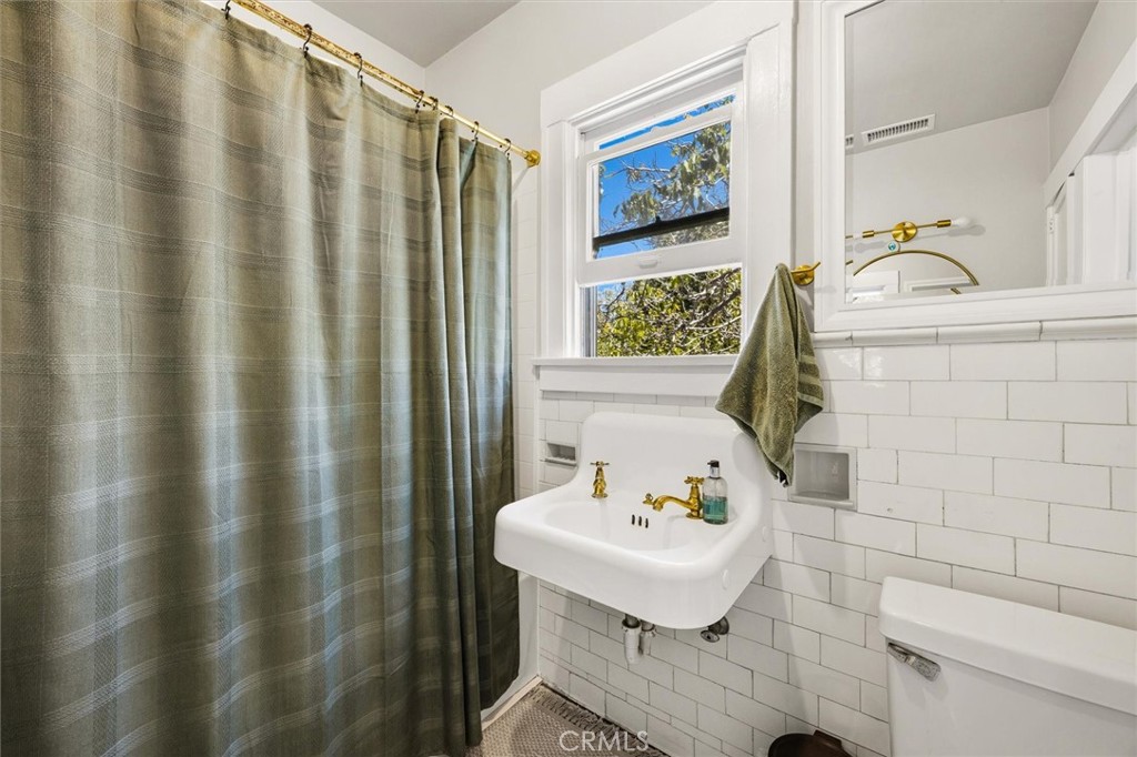 Bathroom with white subway tile, a brass-fitted pedestal sink, and an olive shower curtain.