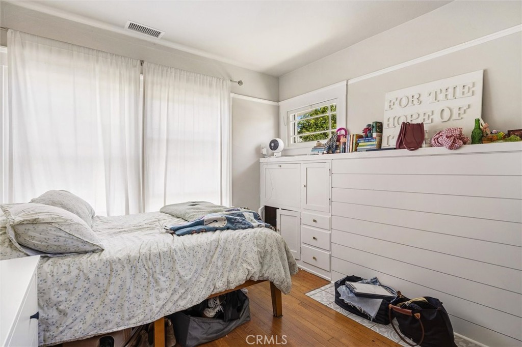 Bedroom with pale floral bedding, sheer curtains, and a large built-in white dresser.