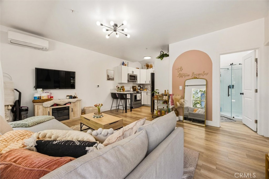 Open-plan living room and kitchen with a gray sectional, wood floors, and blush-pink arched accent wall.