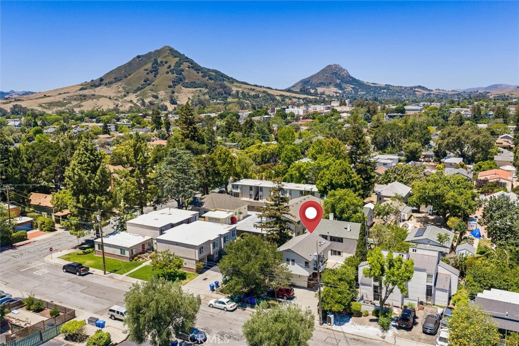 Aerial view of a pinned home in a tree-lined neighborhood below dry rolling hills.