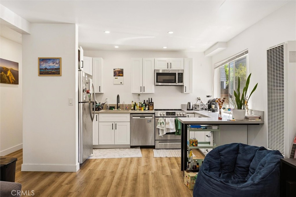 Kitchen with white cabinets, stainless steel appliances, a breakfast bar, and wood-look floors.