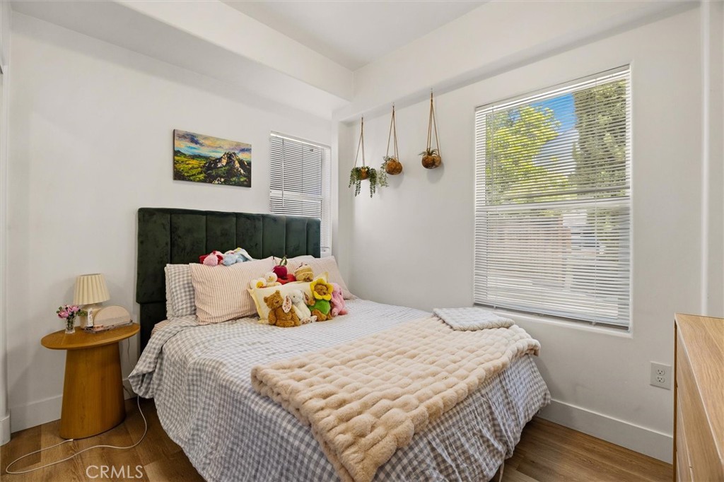Bedroom with a dark green headboard, checked bedding, hanging plants, and two bright windows.
