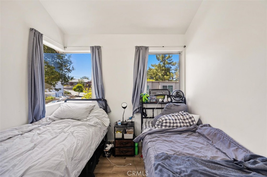 Bedroom with two single beds, gray curtains, and daylight coming through two windows.