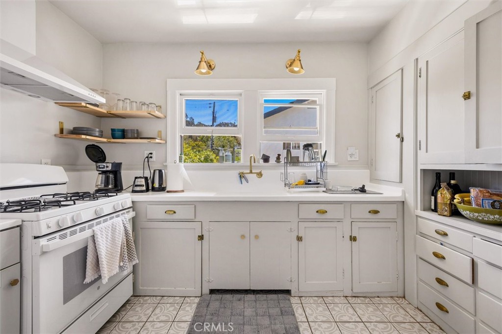 White kitchen with patterned tile floors, open shelves, and a double sink beneath two windows.