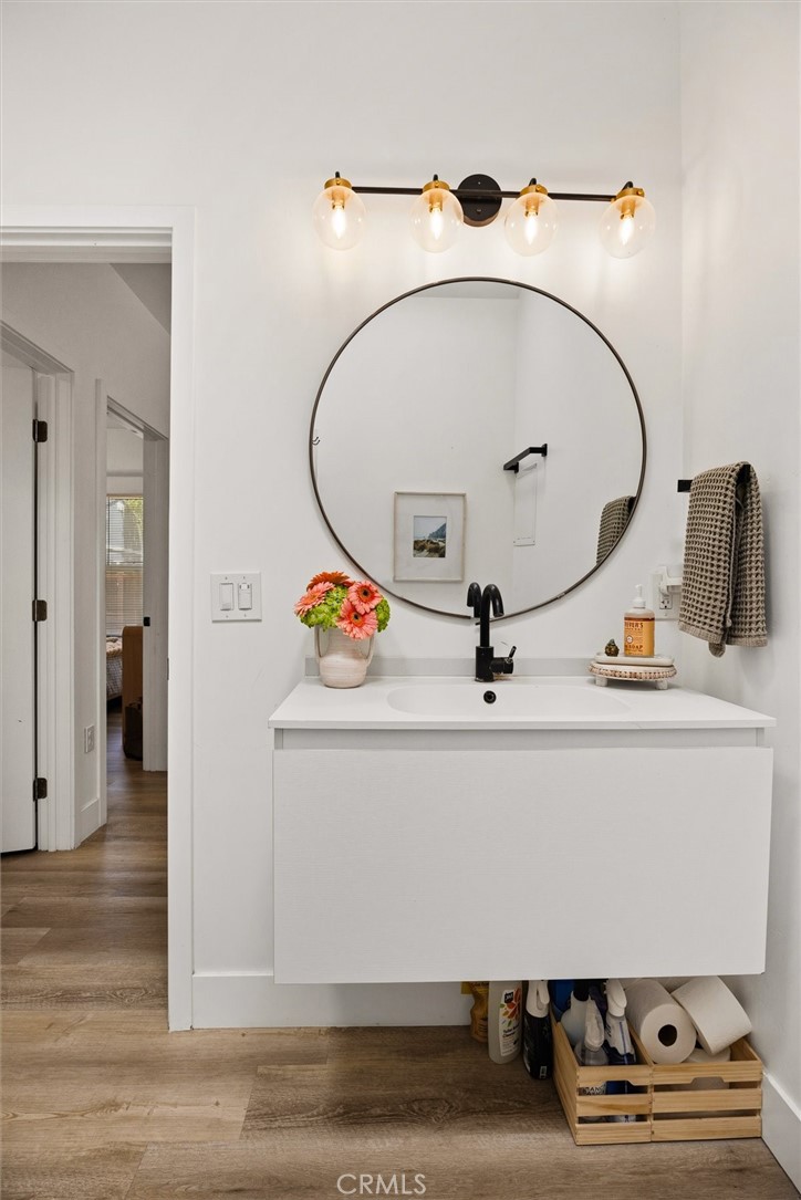 Bathroom vanity with a round mirror, black faucet, and brass four-light fixture.