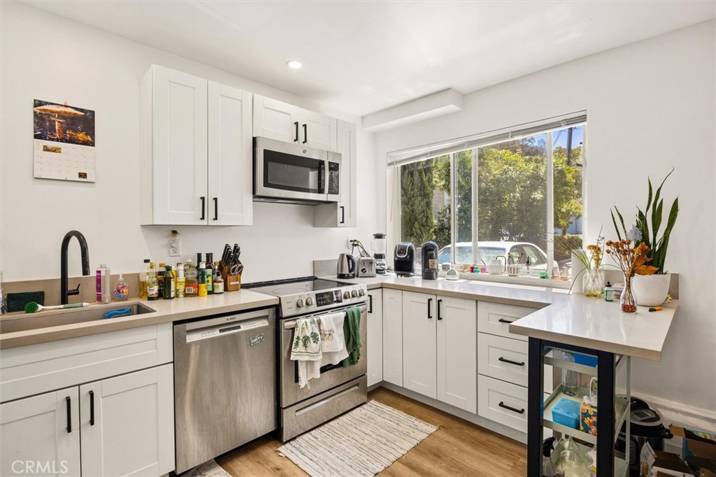 Bright white kitchen with stainless appliances, a large window overlooking greenery, and a white island counter.