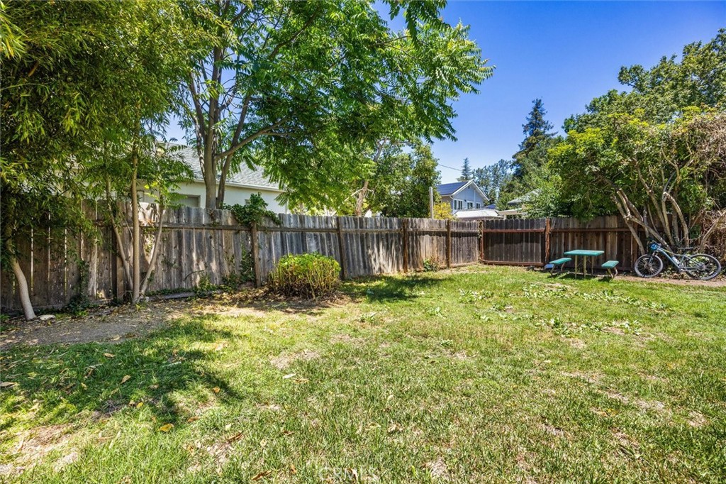 Backyard with a grassy lawn, mature trees, wooden privacy fence, and outdoor table and benches.