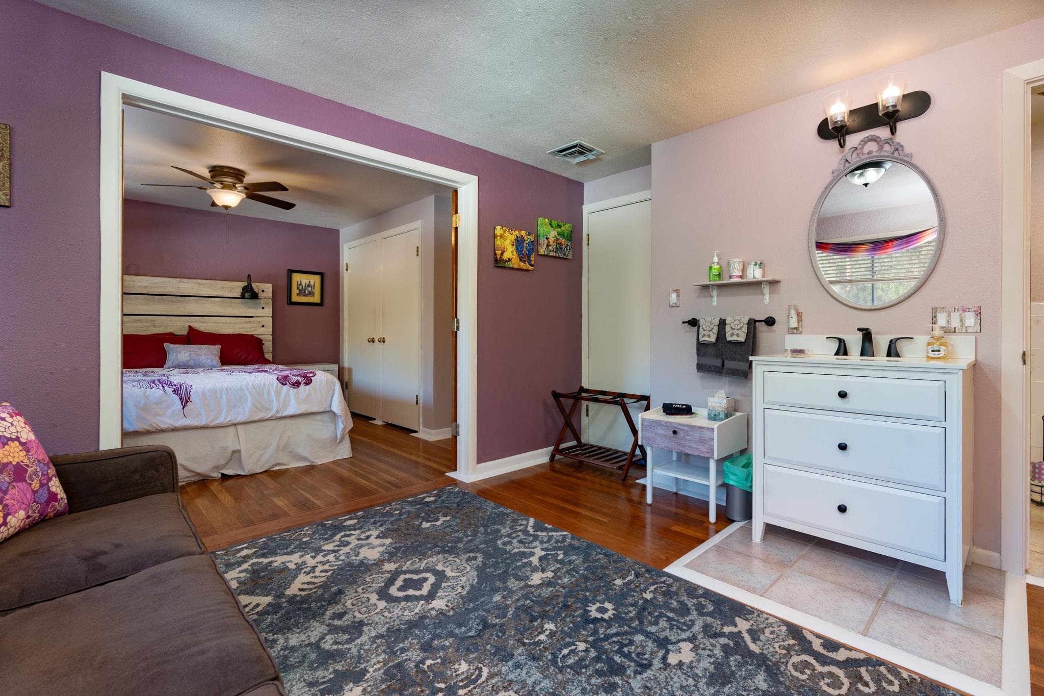 Bedroom with purple walls, a wood headboard, and an adjoining white vanity with a round mirror.