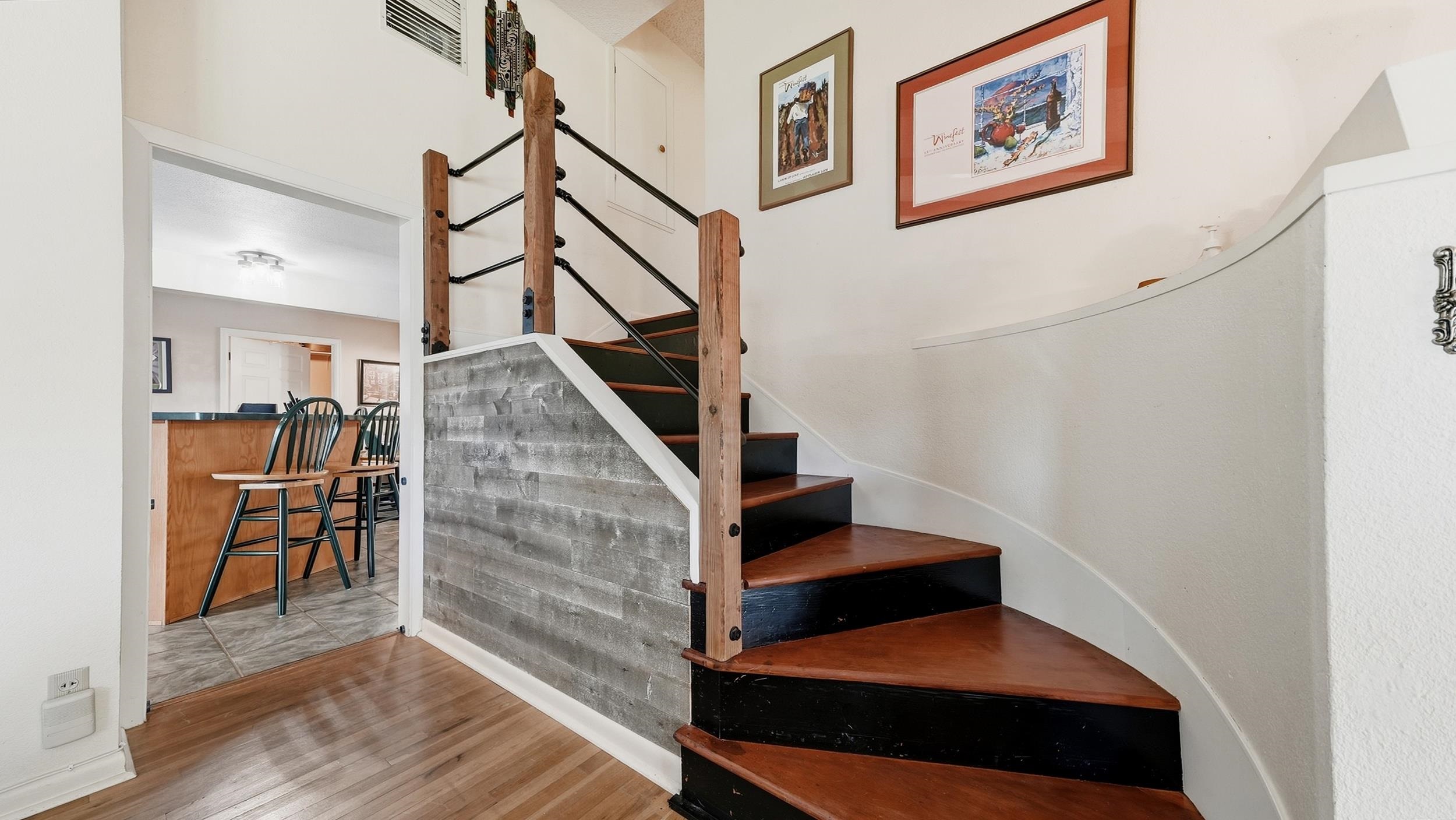 Curved wood-and-black staircase with rustic railings and a gray tile half wall beside a dining area.
