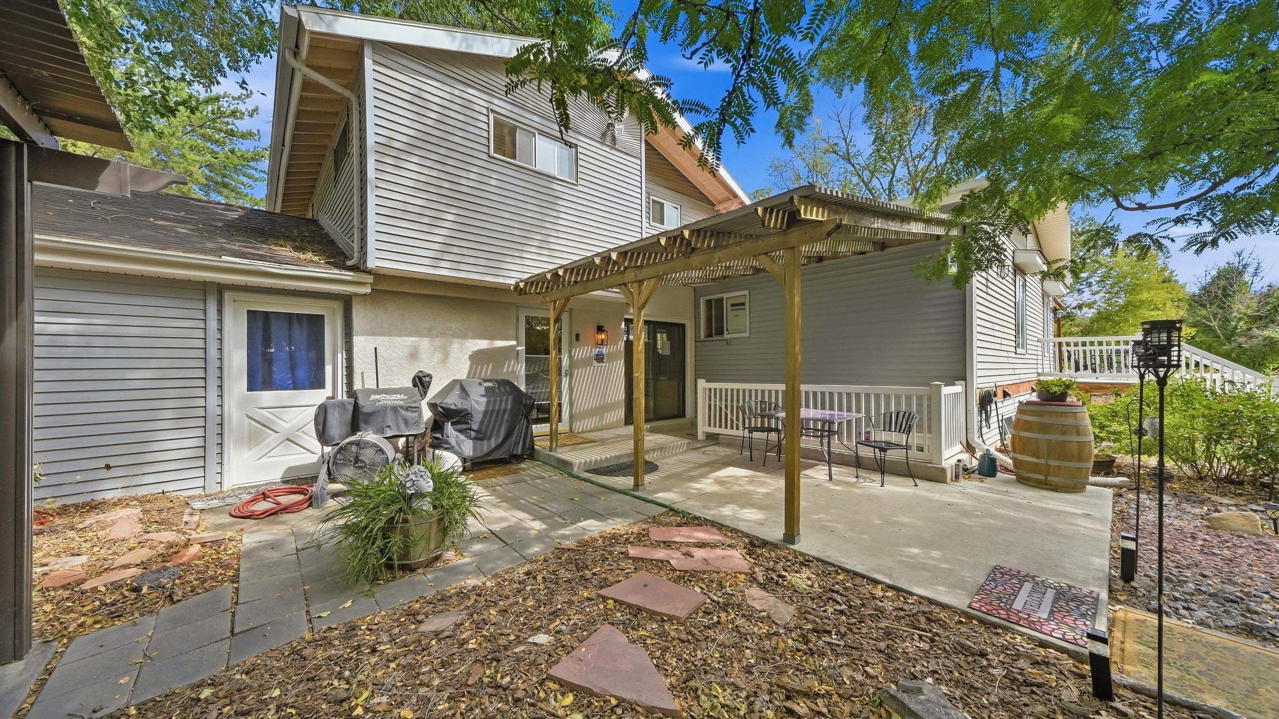 House’s rear patio with a wooden pergola, outdoor dining set, and covered grills.
