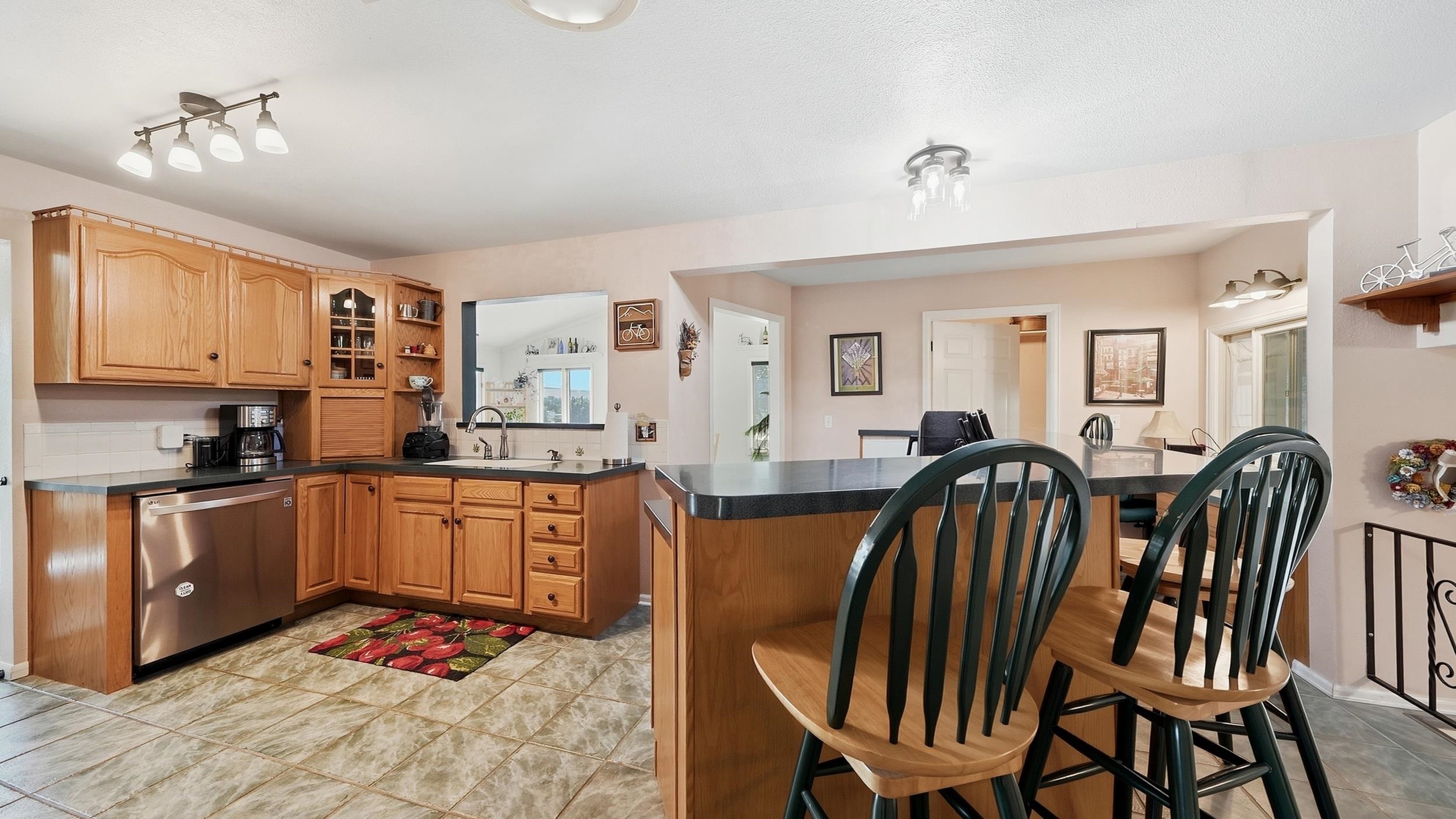 Kitchen with wood cabinets, tiled floors, and a breakfast bar lined with dark chairs.