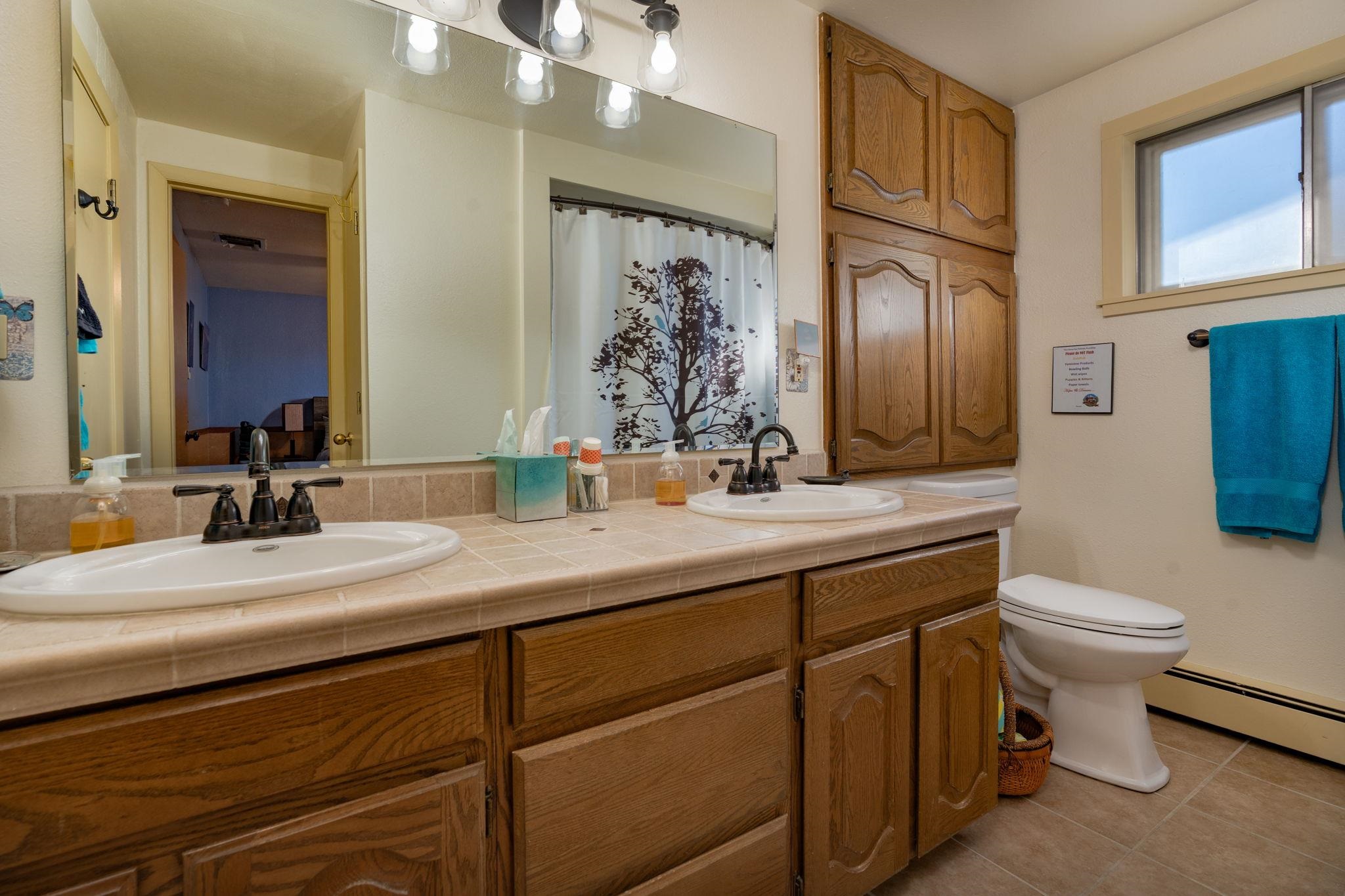 Bathroom with a double-sink vanity, warm wood cabinets, and a toilet beside a window.