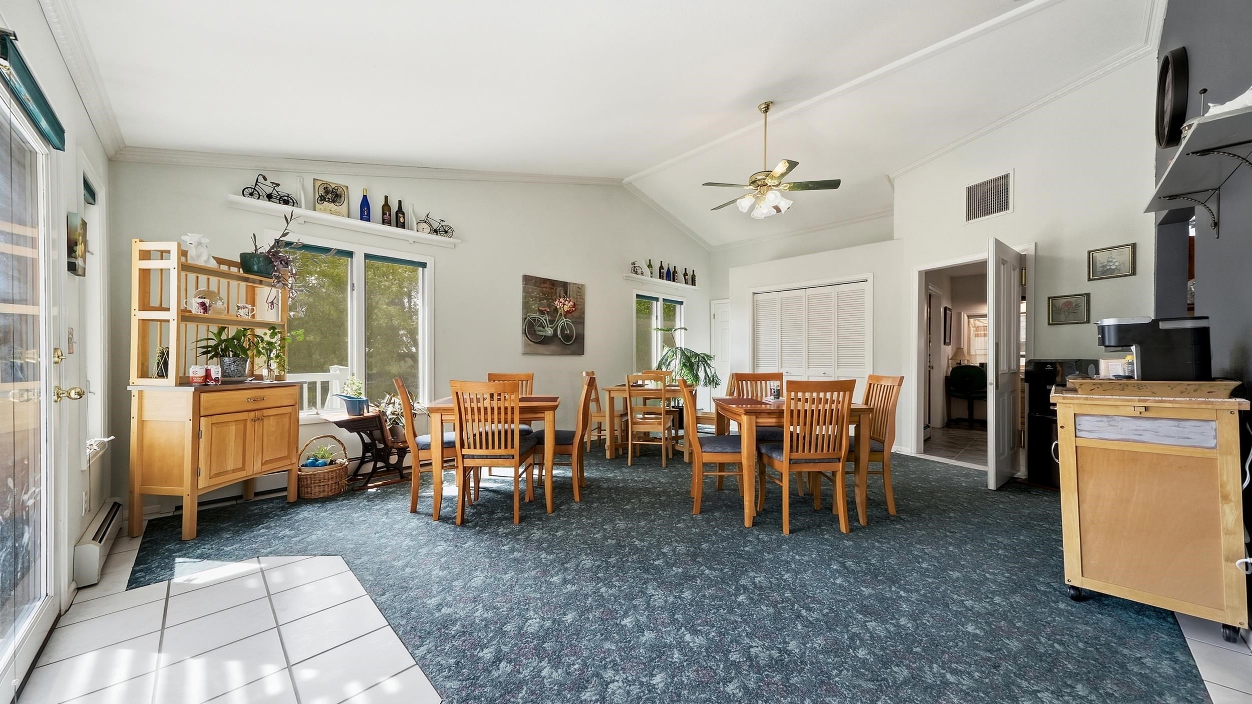 Dining room with two wooden table sets, large windows, and blue patterned carpet.