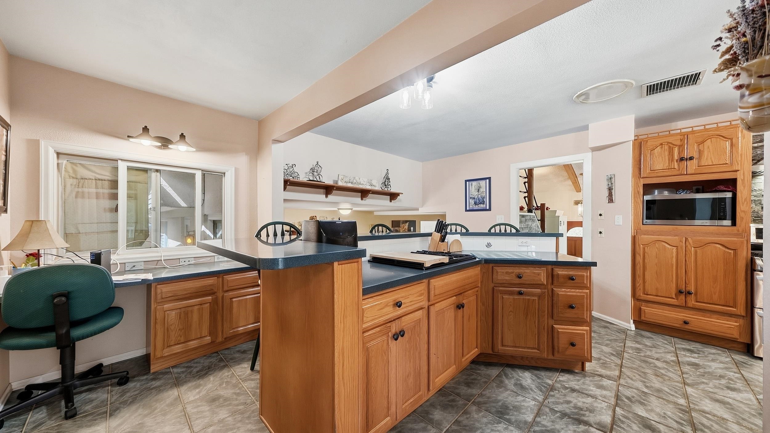 Kitchen with wood cabinetry, dark countertops, and a central island.