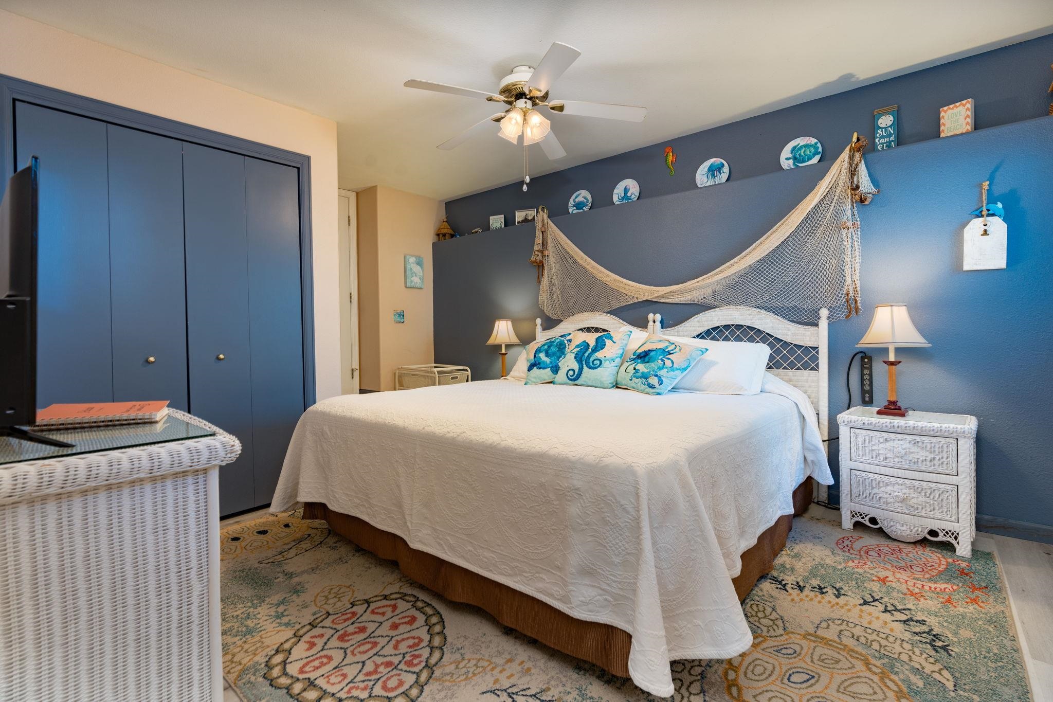 Bedroom with a white bed, blue ocean-themed walls, a decorative fishing net, and colorful rugs.