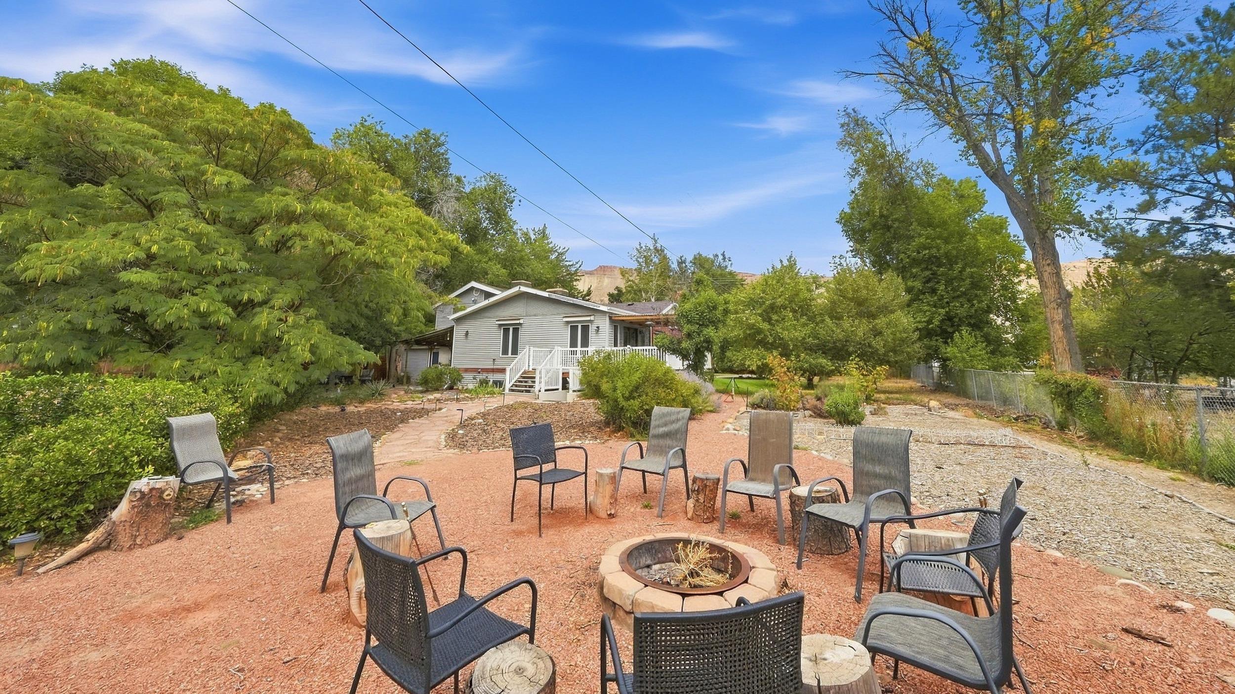 Backyard seating area with a circular stone fire pit, outdoor chairs, and a raised deck behind the home.