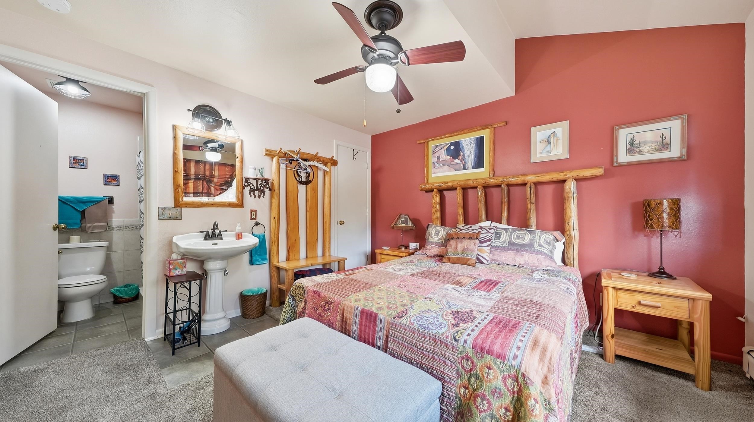 Bedroom with a rustic log bed, patchwork quilt, red accent wall, and open attached bathroom.