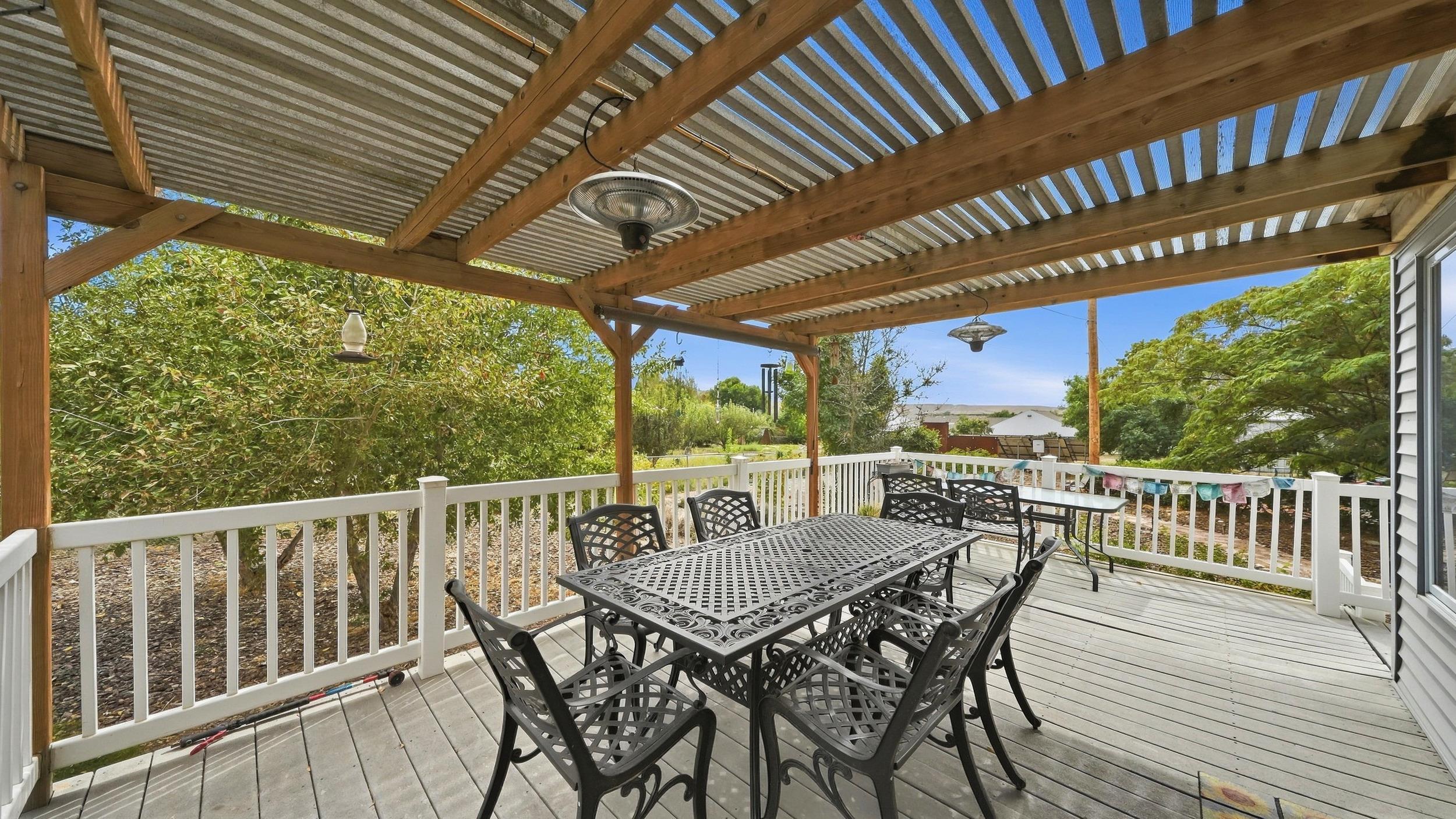 Covered deck with a black metal dining set beneath a timber pergola.