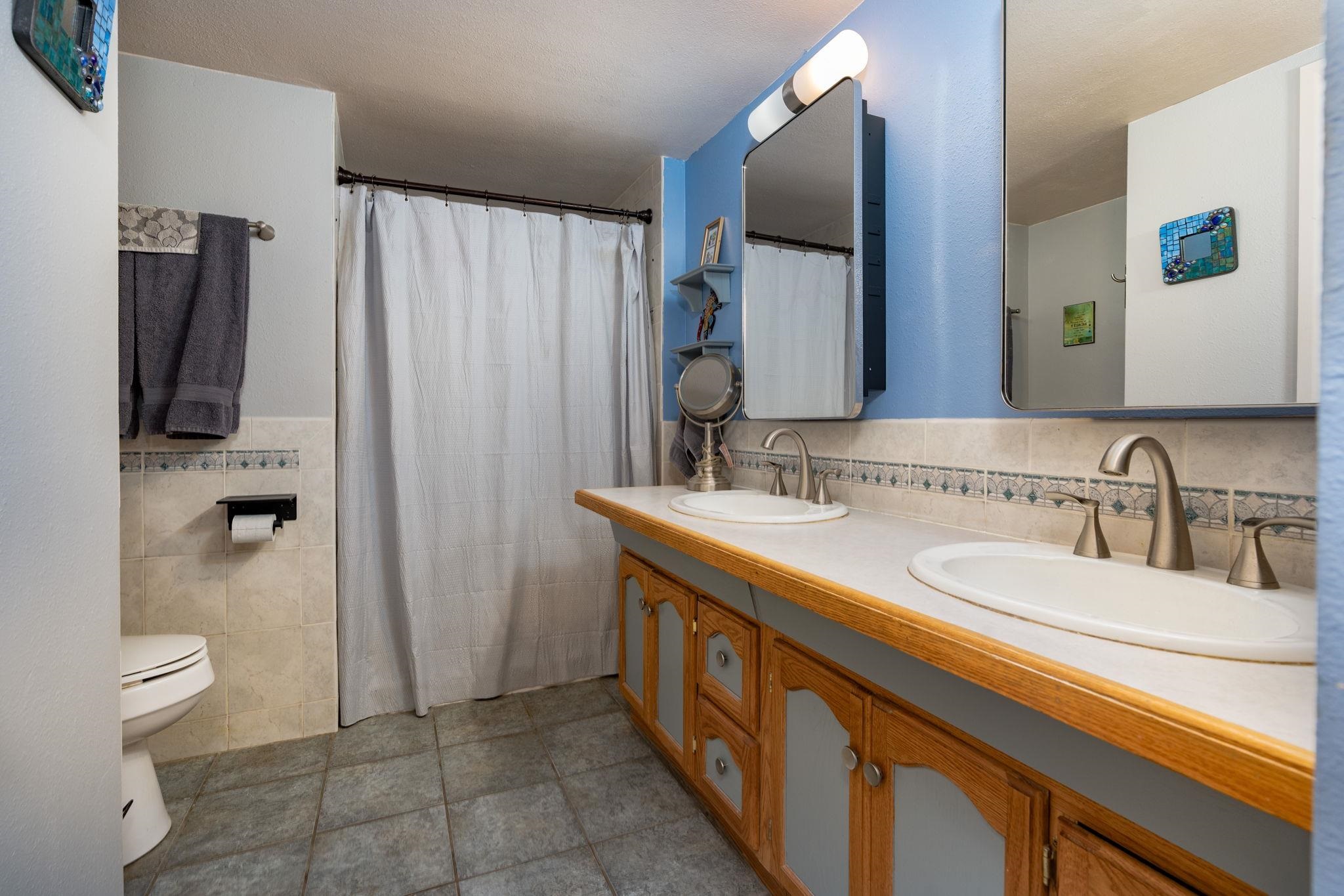 Bathroom with a long wood vanity, two sinks, large mirrors, and a blue accent wall.