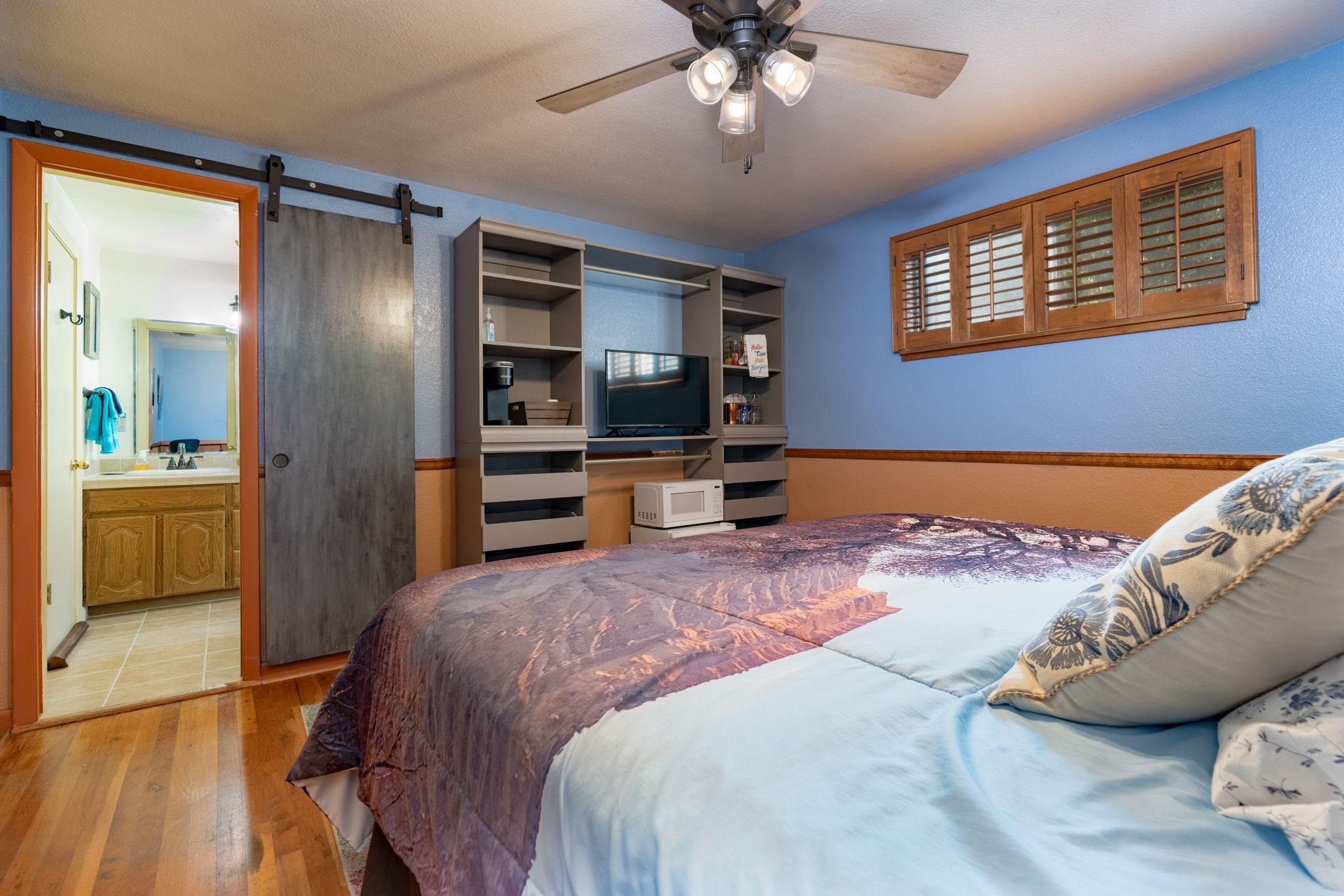 Bedroom with a large bed, blue walls, built-in TV shelving, and a sliding barn door to the bathroom.
