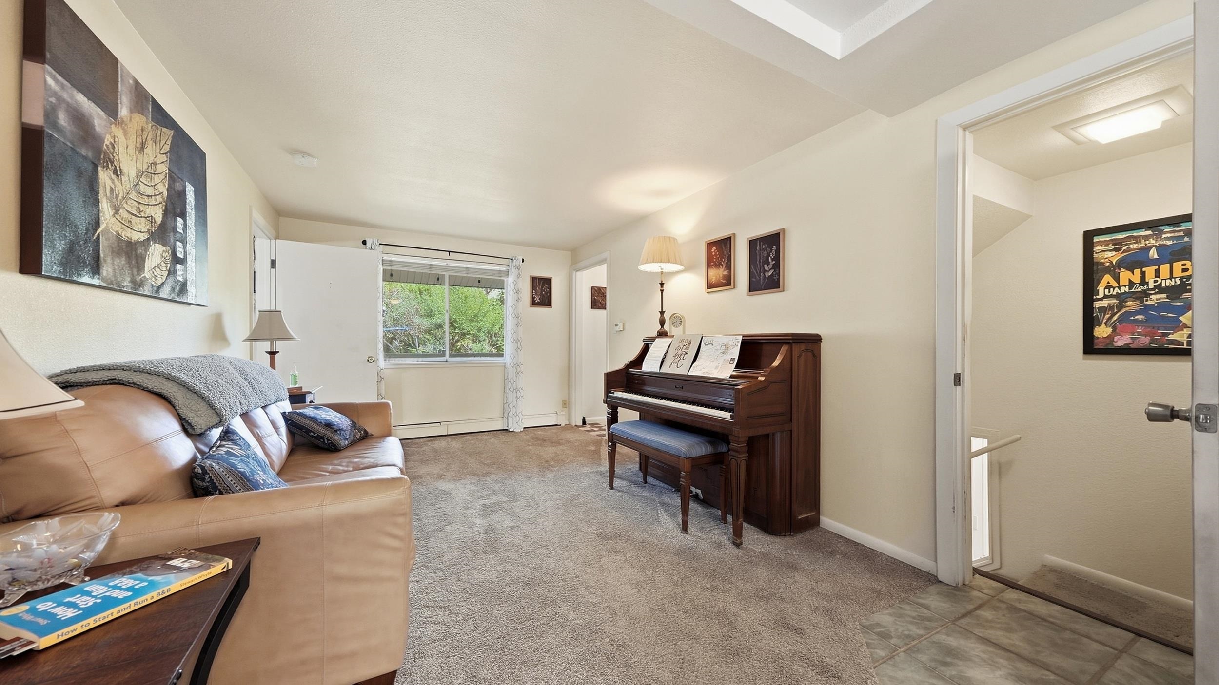 Living room with a tan leather sofa and upright piano beside a sliding glass door.