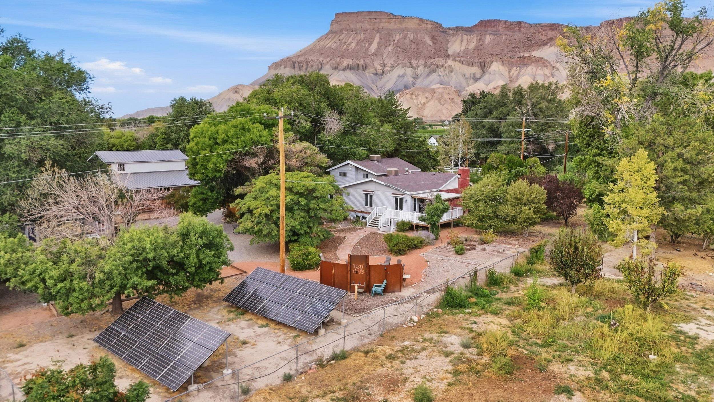 Rural home with solar panels and detached outbuilding beneath red-rock cliffs